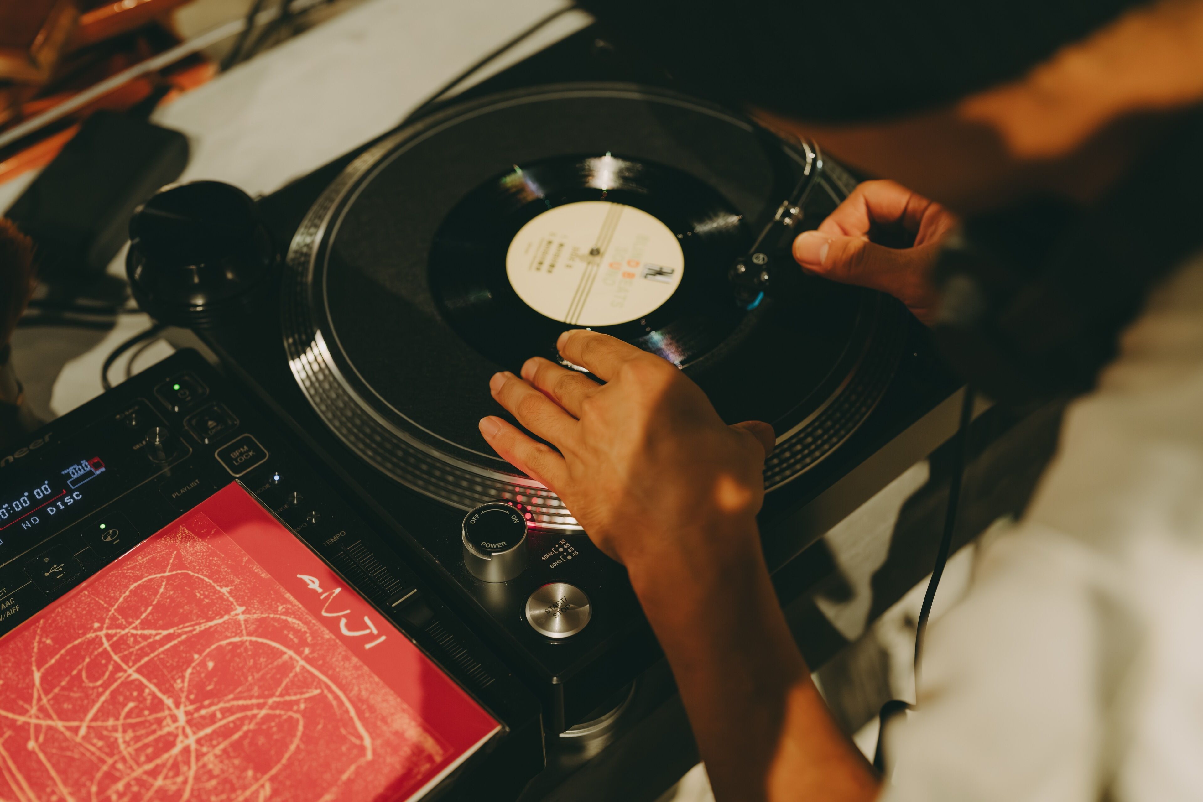 Primer plano de un tocadiscos con un disco de vinilo, un mezclador y una tarjeta roja con garabatos.
