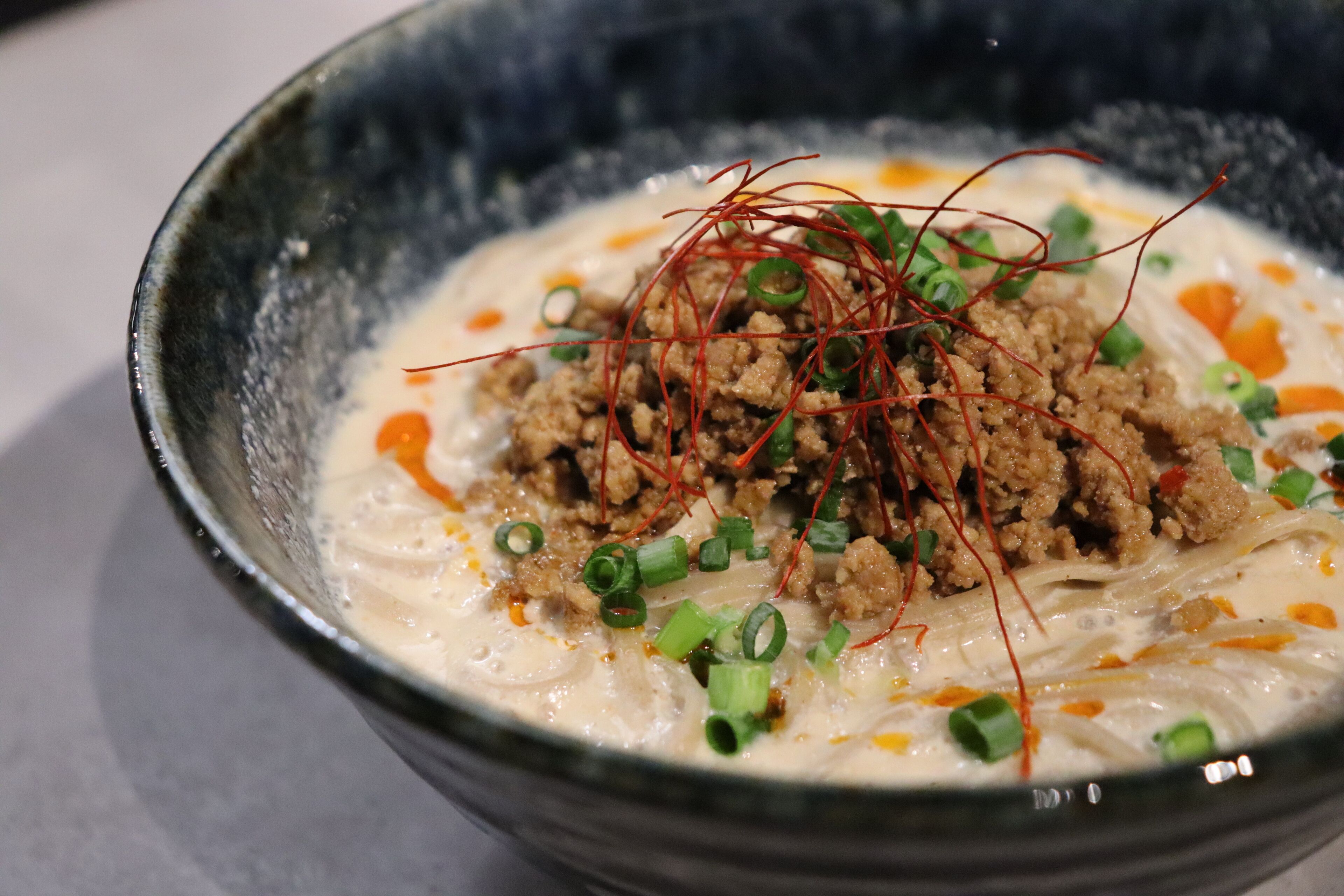 Eine Schüssel Suppe mit Hackfleisch, grünen Zwiebeln und roten Fäden darauf.