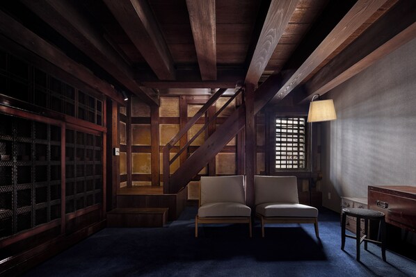 Una habitación con techo de madera, una escalera, un sofá, una mesita y una lámpara.