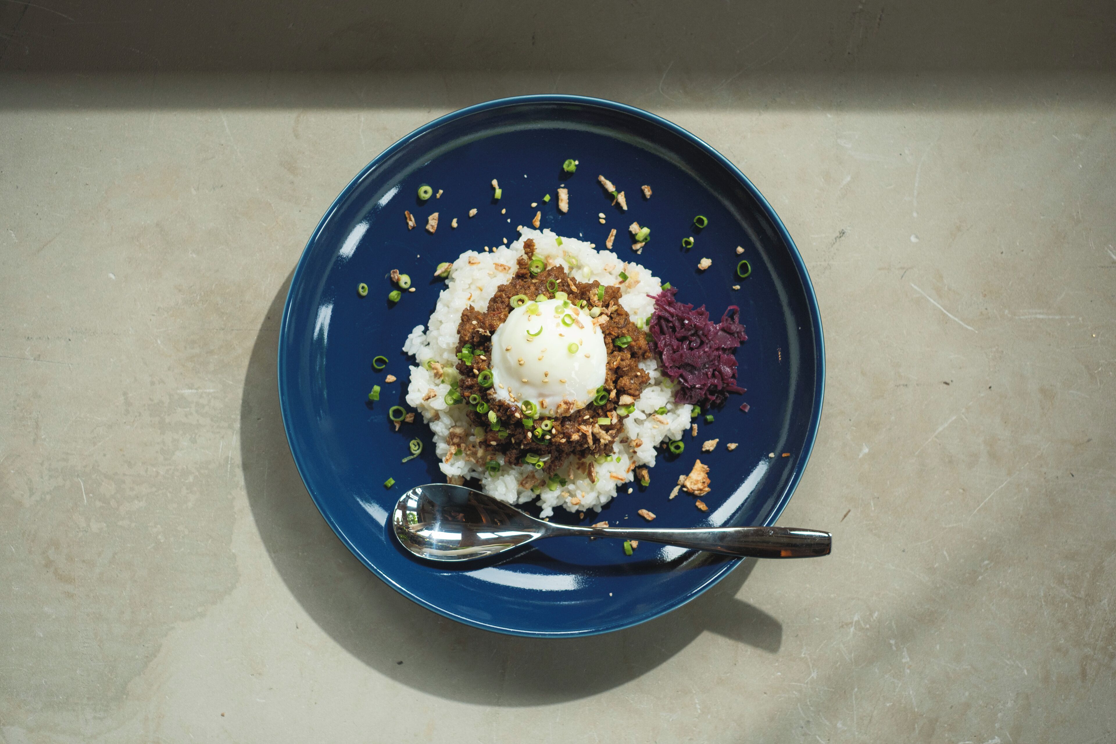 A blue plate with a white dessert, green garnish, and a spoon on a beige surface.