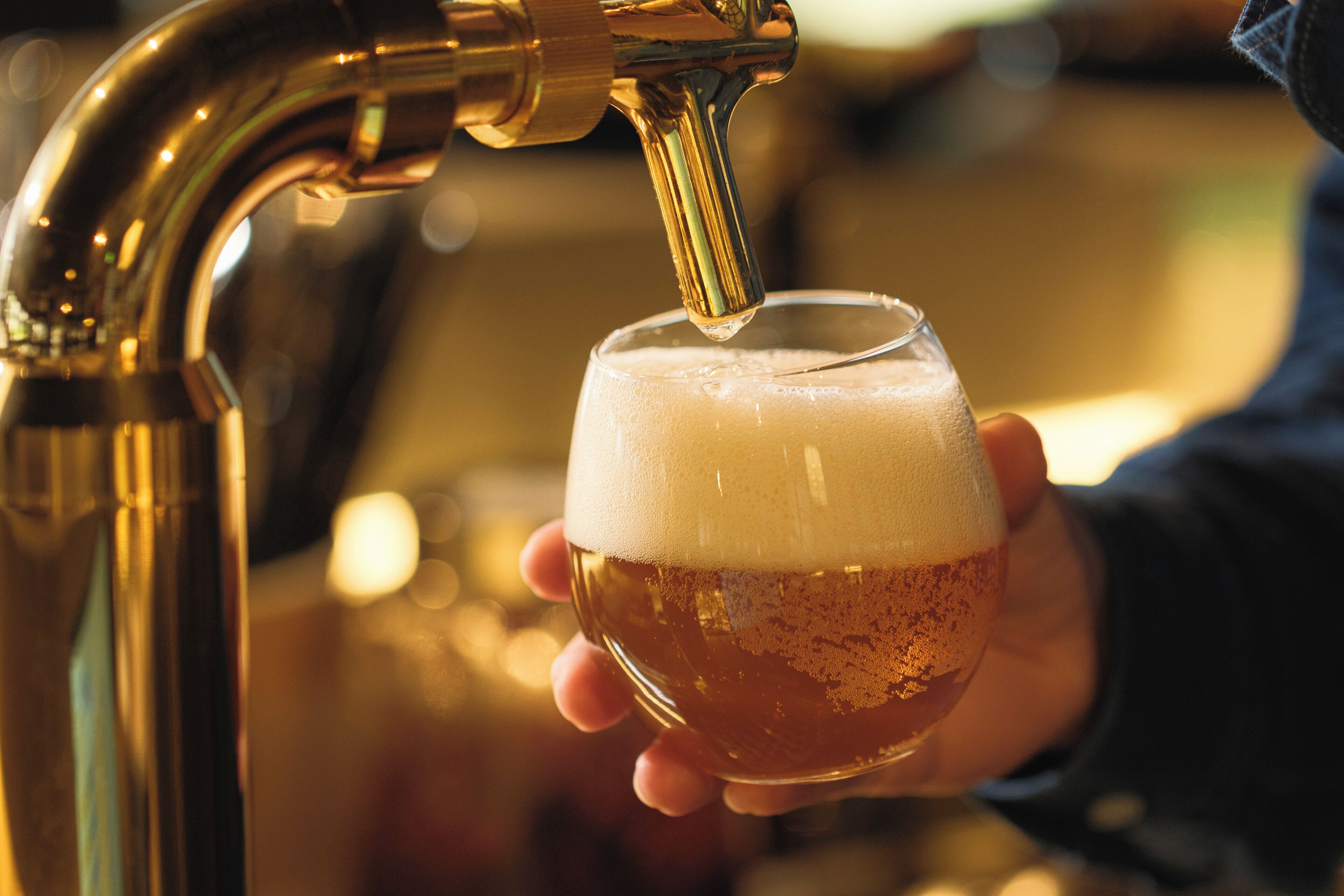 A hand holding a glass of beer with a tap pouring into it.