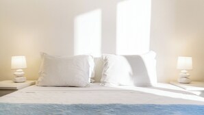 A neatly made bed with white linens and pillows, two bedside lamps, and a blue textured rug.
