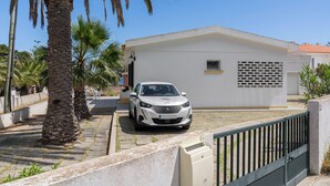 A white car parked in front of a building with a flat roof and a small window.