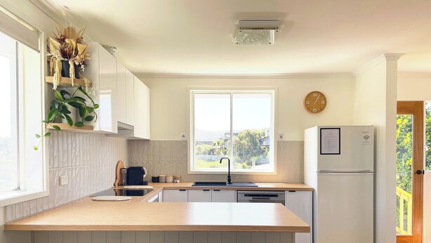 A modern kitchen with a large window, a built-in island with stools, and a refrigerator. - Quarry House - Bright and Renovated, near Hobart (Mornington)