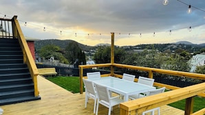A wooden deck with a glass-top table and white chairs, overlooking a green landscape and distant buildings. - Quarry House - Bright and Renovated, near Hobart (Mornington)
