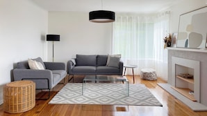 A modern living room with a grey sofa, a glass coffee table, a black floor lamp, and a fireplace with a white mantel. - Quarry House - Bright and Renovated, near Hobart (Mornington)