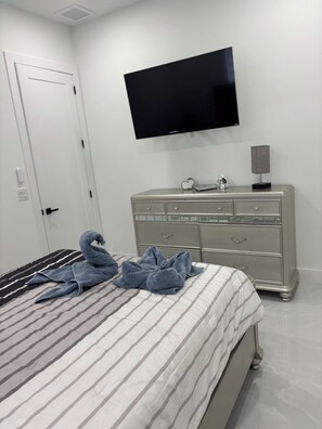 Ein Hotelzimmer mit einem Bett, einem Schminktisch, einem an der Wand befestigten Fernseher und einer Bettdekoration aus Handtüchern in Schwanenform.