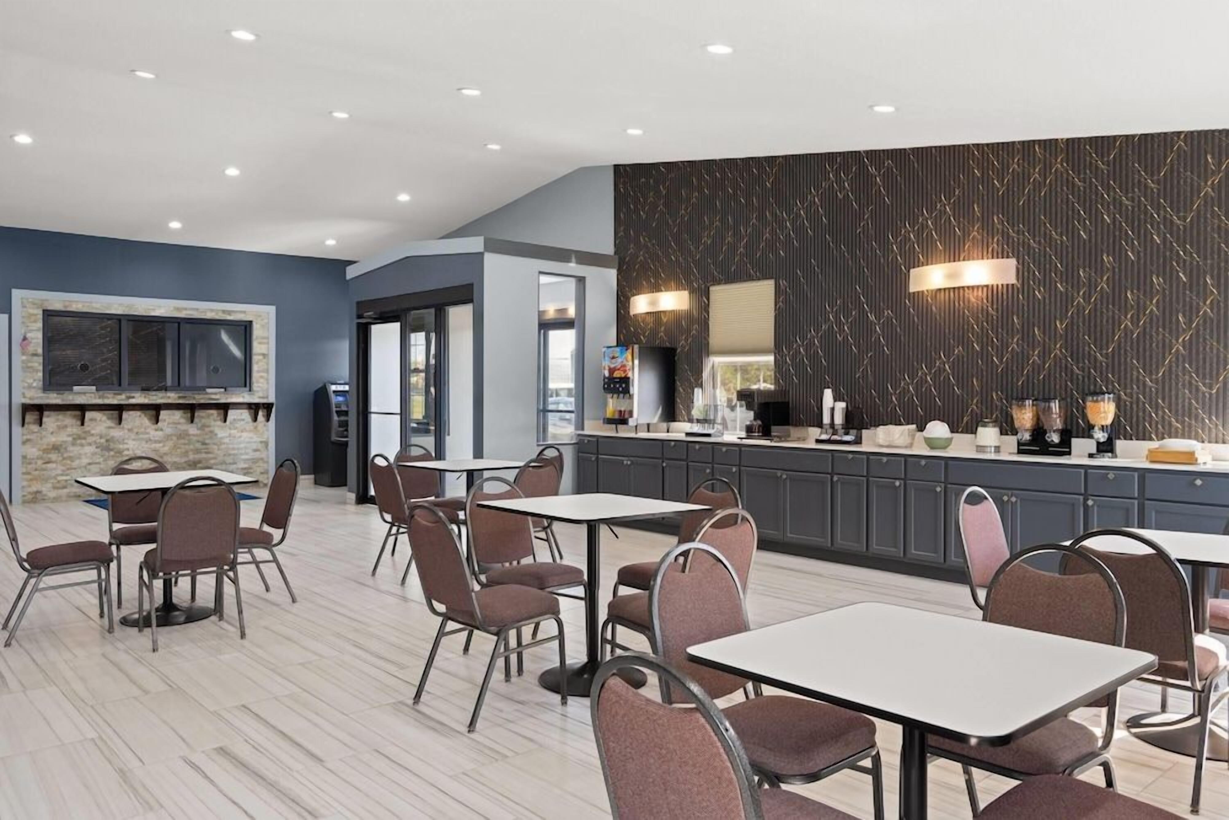 A modern dining area with tables and chairs, a kitchen counter, and a patterned wall.