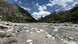 A river with clear water flowing through a rocky landscape, surrounded by mountains and trees.