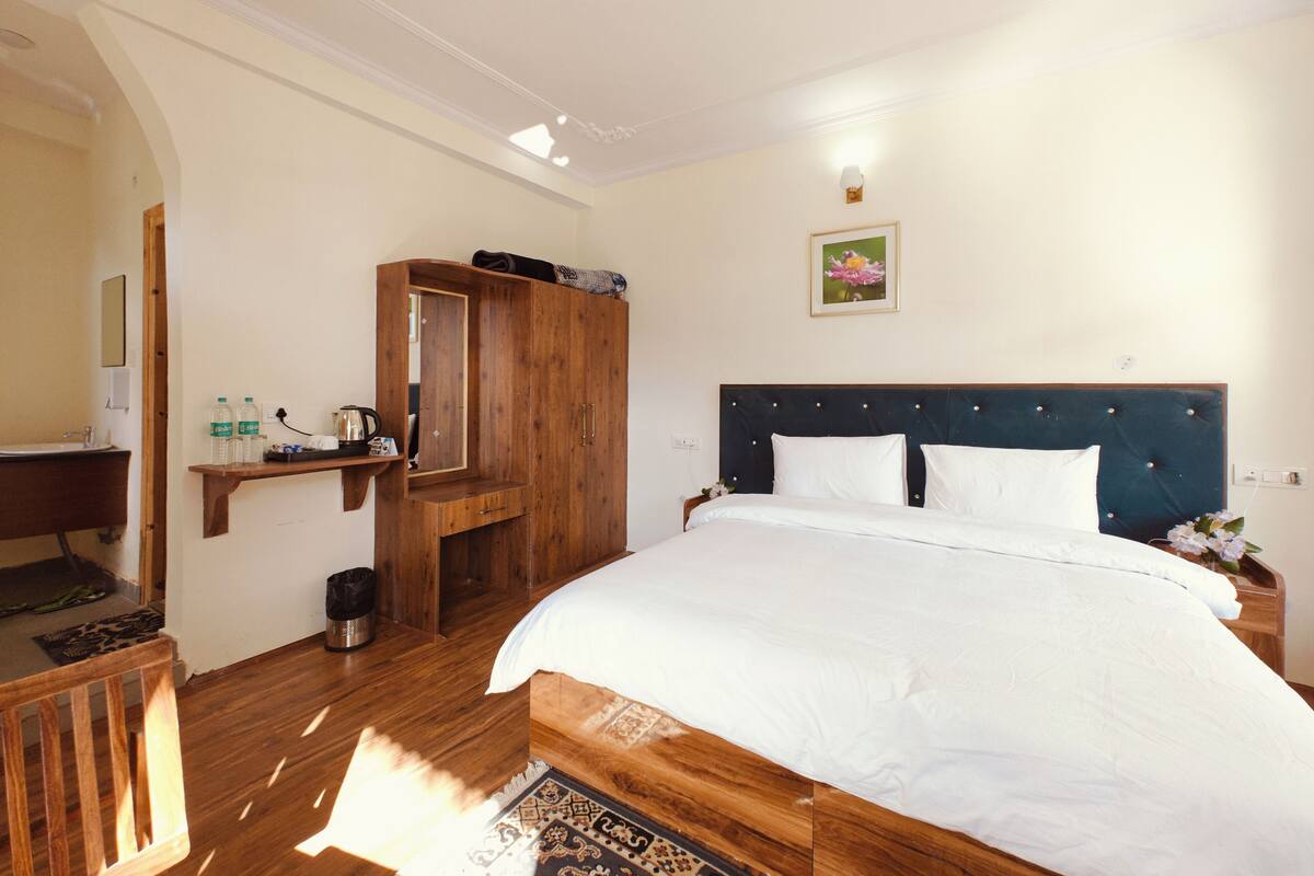 Quarto com cama grande, guarda-roupa de madeira e prateleira pequena com artigos de higiene pessoal.