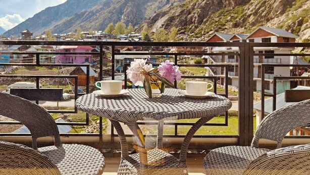 A balcony with wicker furniture, two white cups, and a vase with flowers.