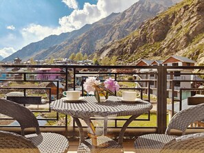 A balcony with wicker furniture, two white cups, and a vase with flowers. - Hotel Chitkul (Chitkul)