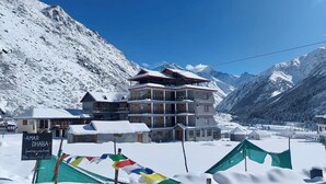 A multi-story building with a snow-covered roof, surrounded by snow-covered mountains.
