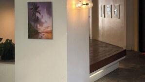 Un couloir avec un mur blanc, un tableau représentant un coucher de soleil encadré et un luminaire.