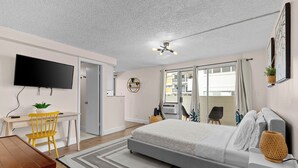 Une chambre moderne avec un lit, un bureau, une chaise, une télévision et une grande fenêtre.