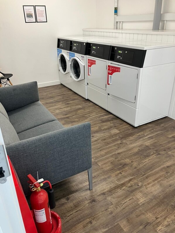 A laundry room with a grey sofa, a washing machine, a dryer, and a fire extinguisher.