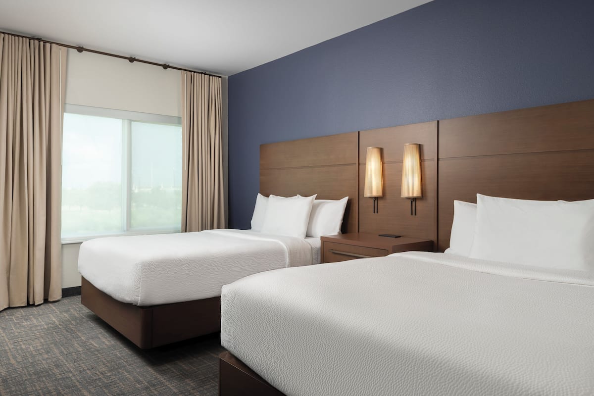 Ein Hotelzimmer mit zwei Betten, einem großen Fenster und einem Nachttisch mit einer Lampe.