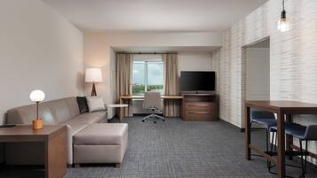 Habitación de hotel con sofá, reposapiés, escritorio, televisor y vistas al exterior.