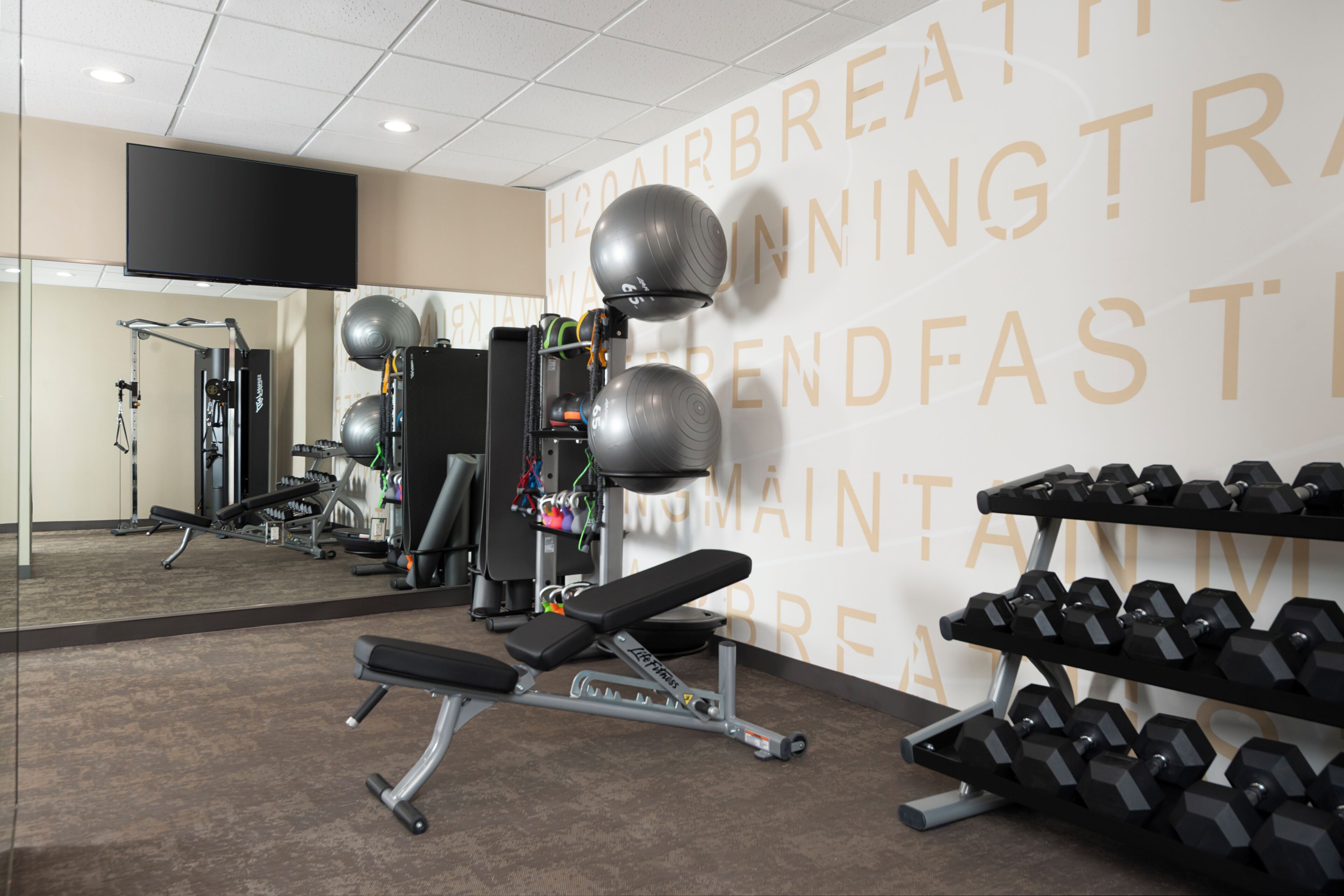 Et fitnessrum med træningsudstyr, en bænk og en væg med motiverende tekst.
