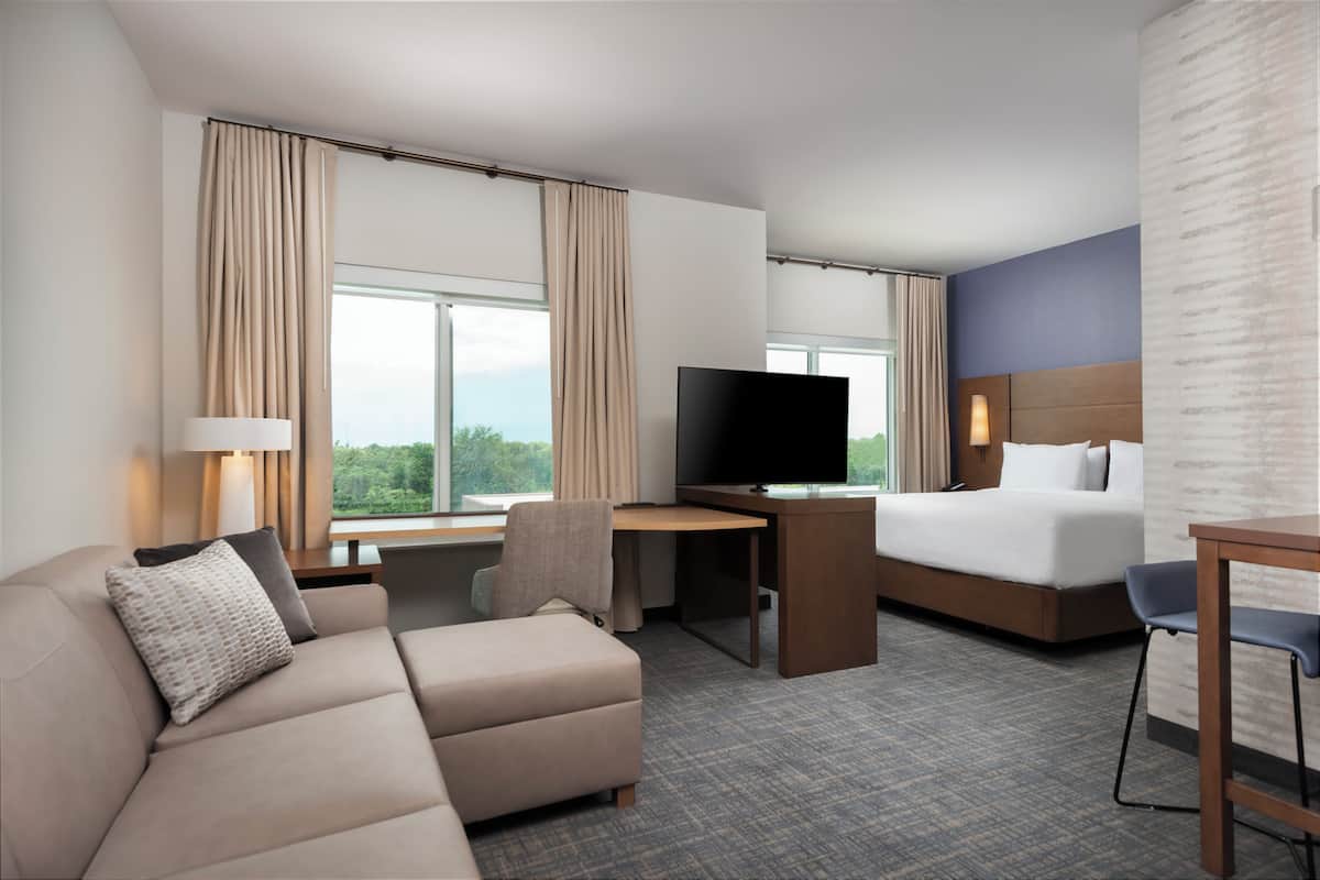 Ein Hotelzimmer mit Bett, Schreibtisch mit Fernseher, Sofa und Sessel.