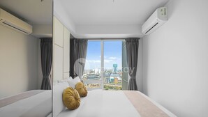 Habitación de hotel moderna con una cama grande, dos almohadas, vistas a la ciudad y un equipo de aire acondicionado.