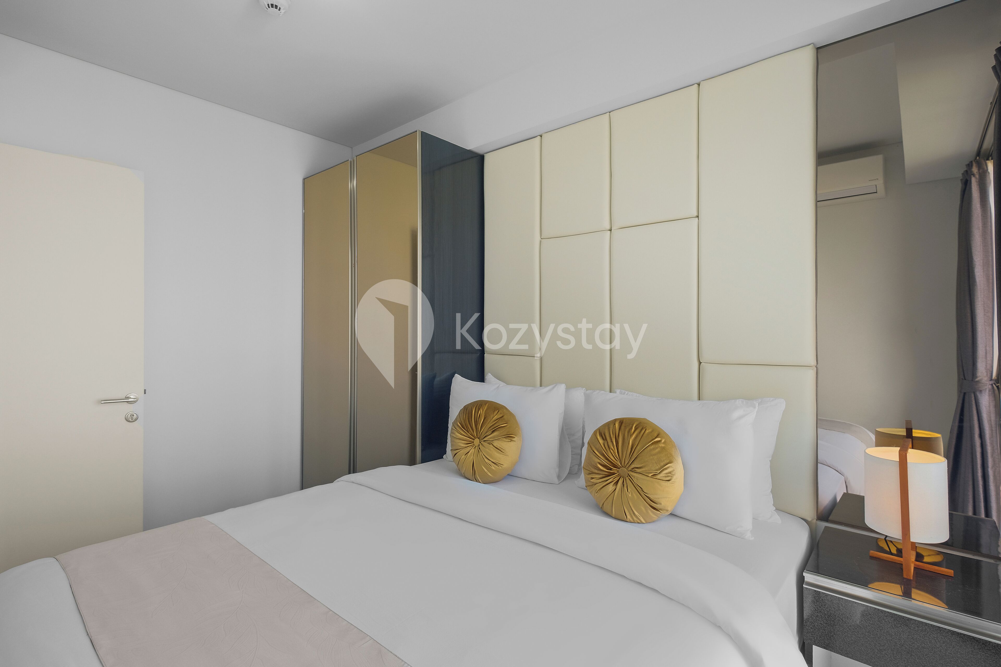 A modern hotel room with a large bed, a bedside table with a lamp, and a large mirror.