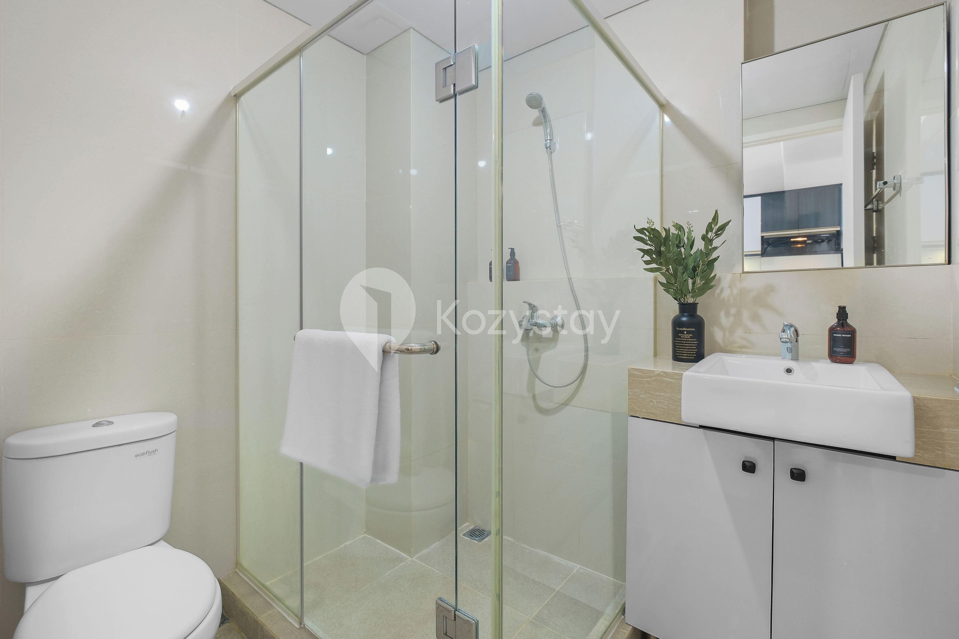 A modern bathroom with a glass-enclosed shower, a white toilet, a sink with a mirror, and a potted plant.