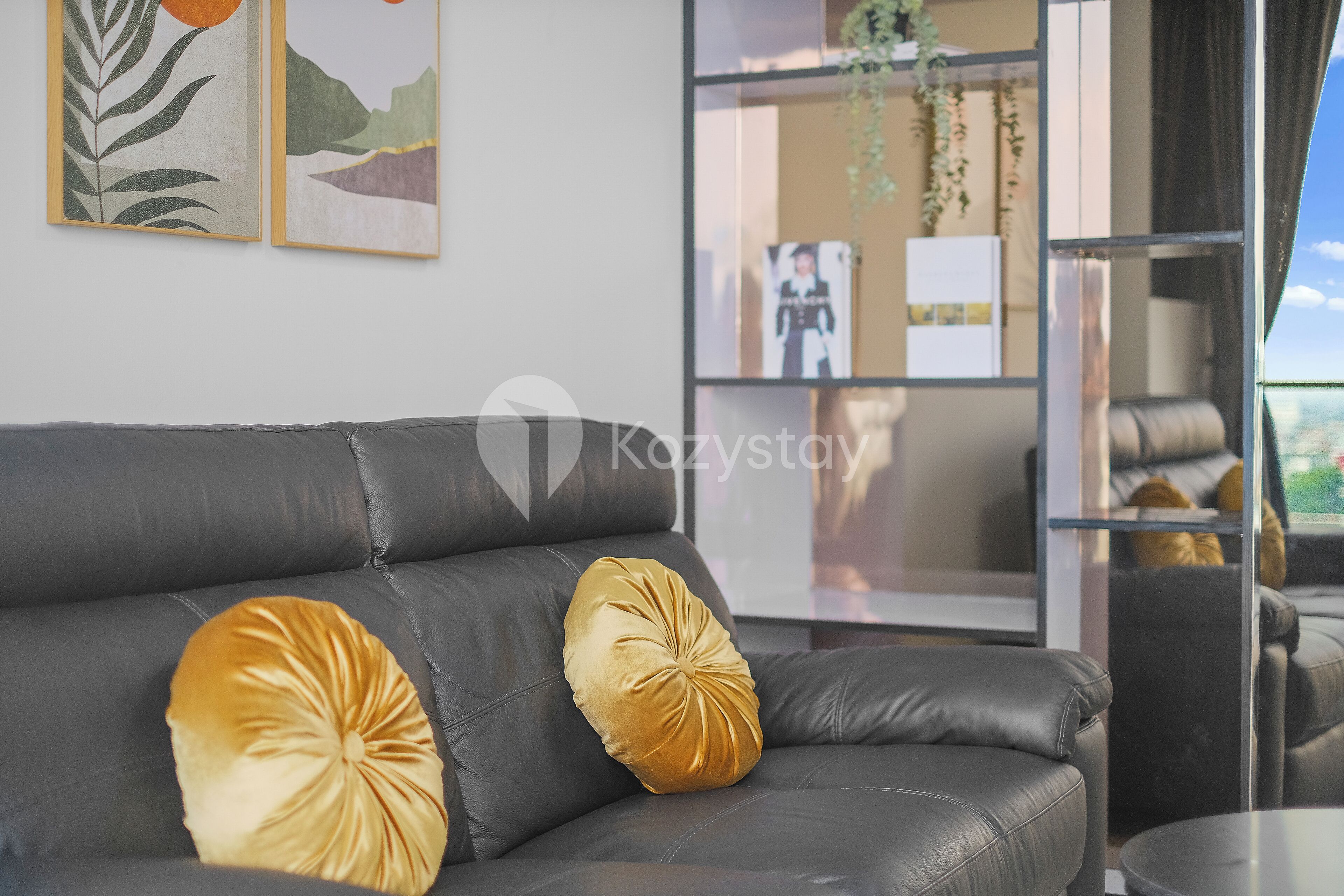 Un salon moderne avec un canapé en cuir noir, deux coussins décoratifs et des œuvres d’art encadrées accrochées au mur.