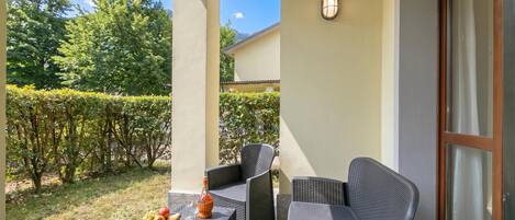 An outdoor patio with wicker furniture, a table with a bottle and fruit, and a magazine.