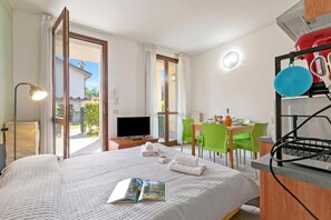 Quarto de hotel com cama, televisão, área de refeições com cadeiras e cozinha equipada com chaleira.