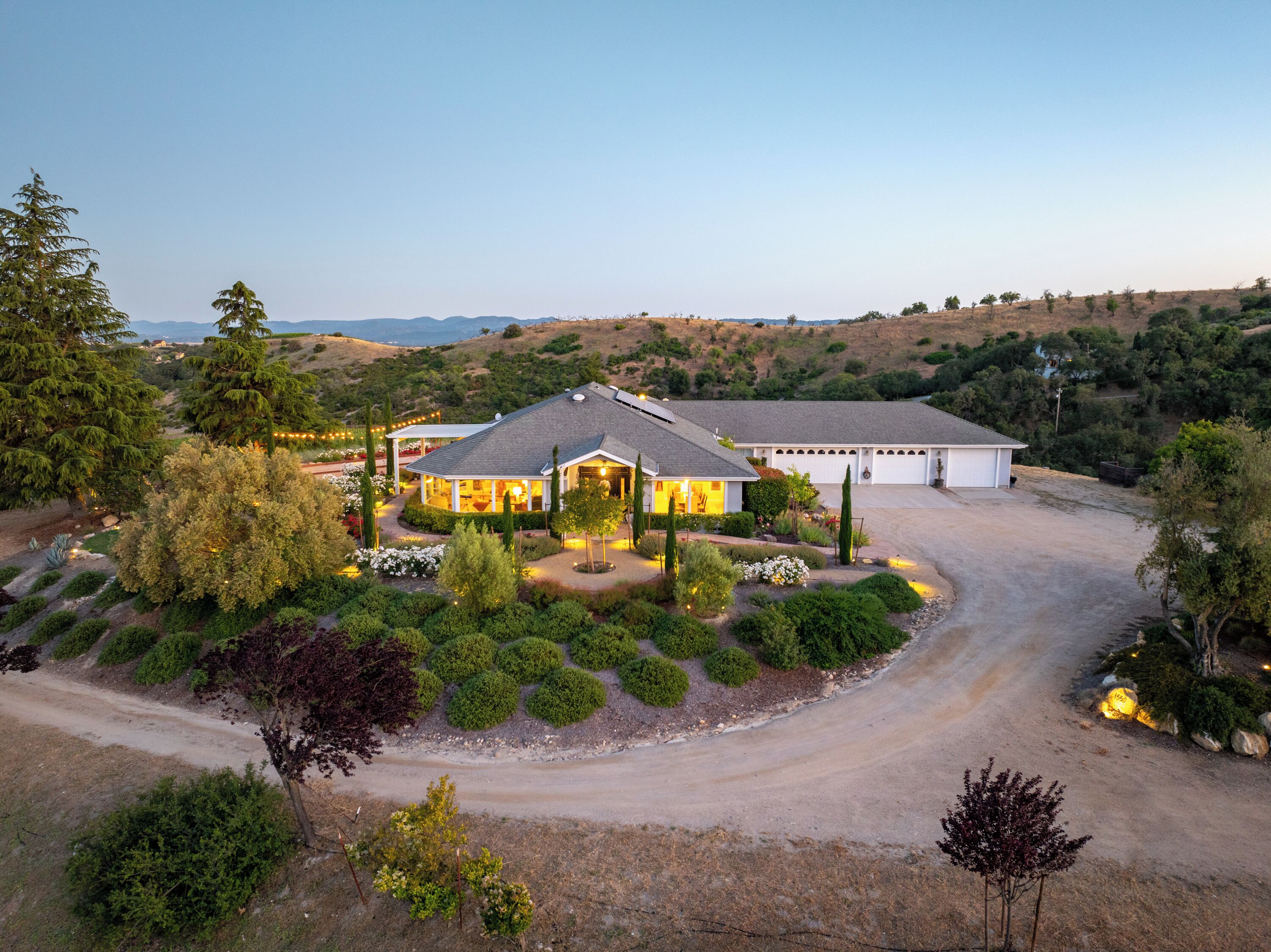 Une grande maison dotée d’une allée spacieuse, entourée de jardins aménagés et d’un paysage vallonné.