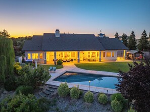 Una casa grande con piscina, mobiliario de exterior y un césped bien cuidado.