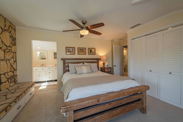 A bedroom with a wooden bed, a stone accent wall, a ceiling fan, and a white closet. - Hidden Acre Vineyard (Paso Robles)