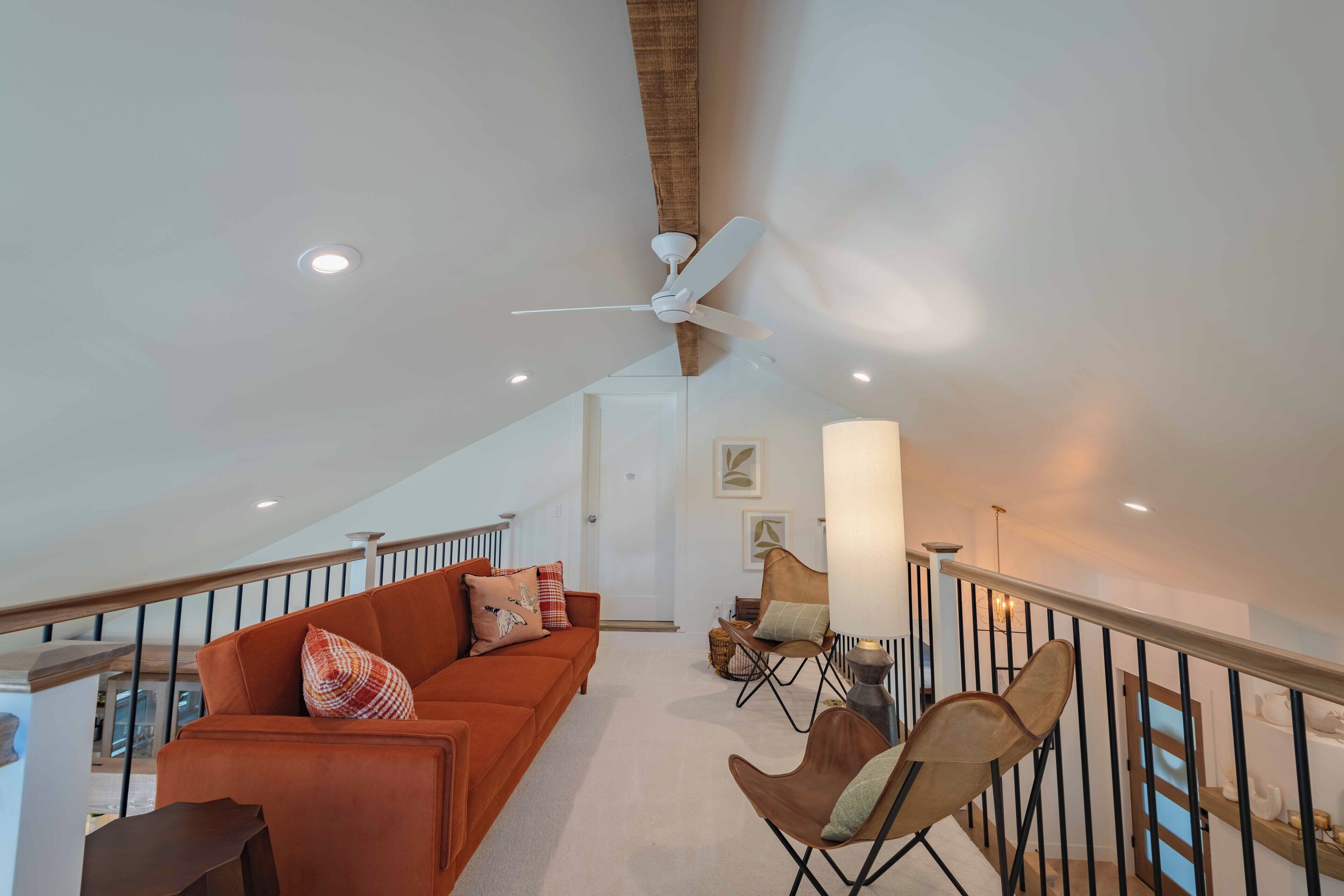 A spacious living area with a high ceiling, a ceiling fan, and a staircase leading to an upper level.