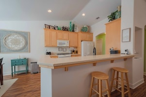 A modern kitchen with wooden cabinets, a large island with stools, a microwave, and a refrigerator.