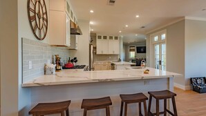 A modern kitchen with a large island, wooden stools, and white cabinetry. - Bella Vita (Paso Robles)