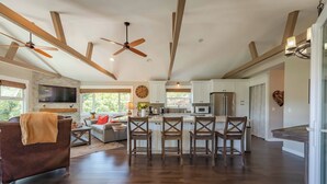 A spacious kitchen with wooden beams, a large island with bar stools, and a dining area with a sofa and coffee table. - Moonglow Cottage (Cambria)