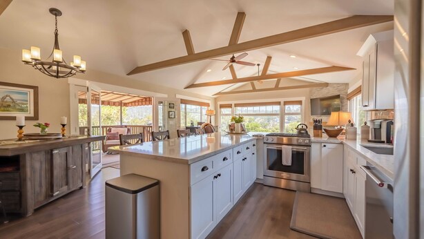 A spacious kitchen with a large island, wooden beams, and a ceiling fan. - Moonglow Cottage (Cambria)