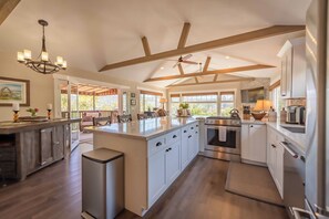 A spacious kitchen with a large island, wooden beams, and a ceiling fan. - Moonglow Cottage (Cambria)