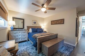 Un dormitorio con cama, cómoda, ventilador de techo, alfombra y un cuadro en la pared.