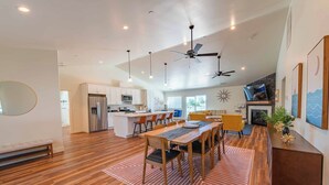 A spacious living area with a wooden floor, a dining table with chairs, a sofa, and a fireplace. There is a kitchen in the background with modern appliances and a large island. - Blue Moon Escape (Paso Robles)