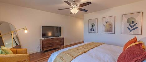 A bedroom with a bed, a ceiling fan, a TV, a dresser, and wall art.