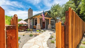 A stone pathway leading to a house with a wooden fence, an American flag, and outdoor seating. - Crafty Oak House (Paso Robles)