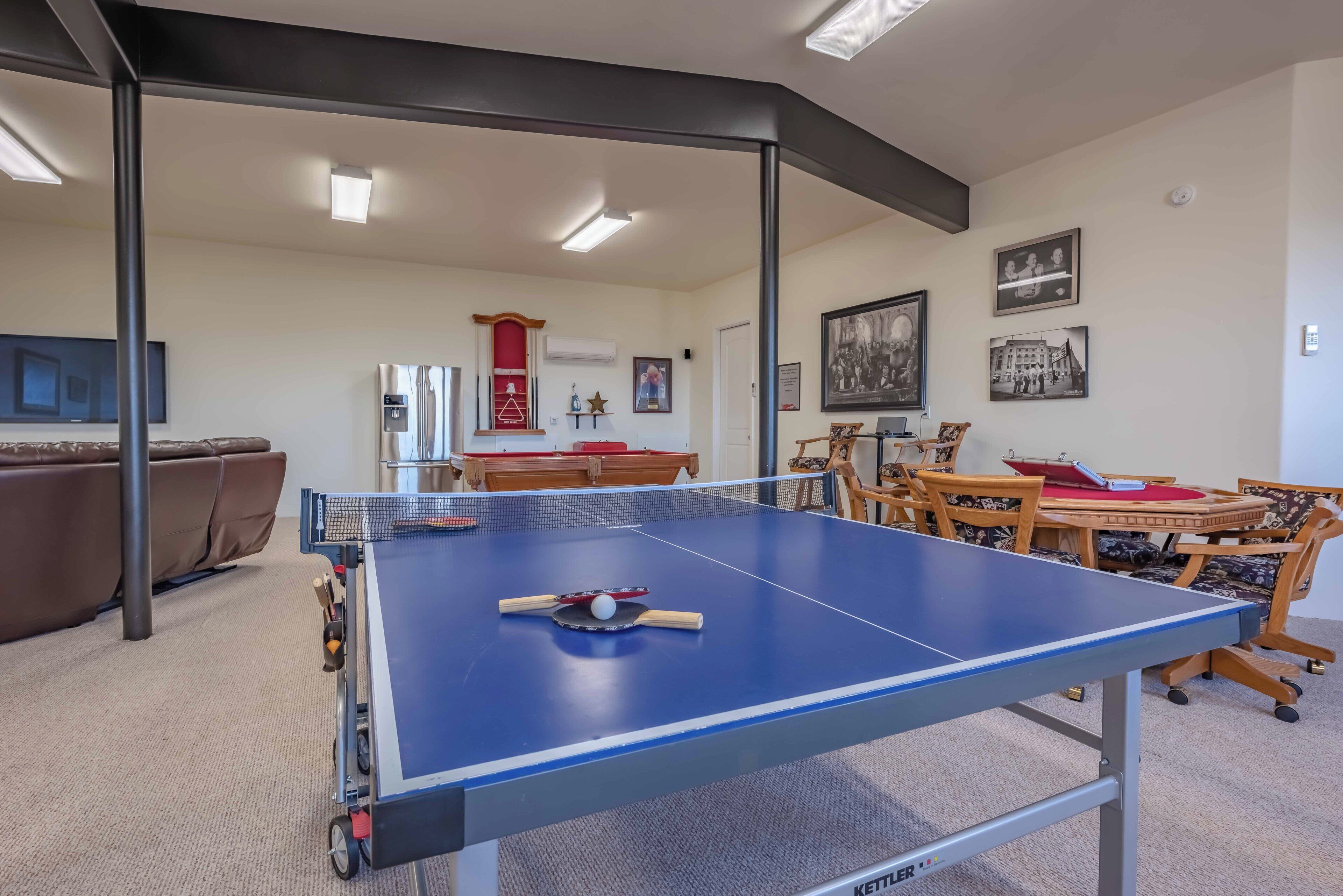 Una mesa de ping pong en una habitación con un sofá, una mesa de madera y sillas.