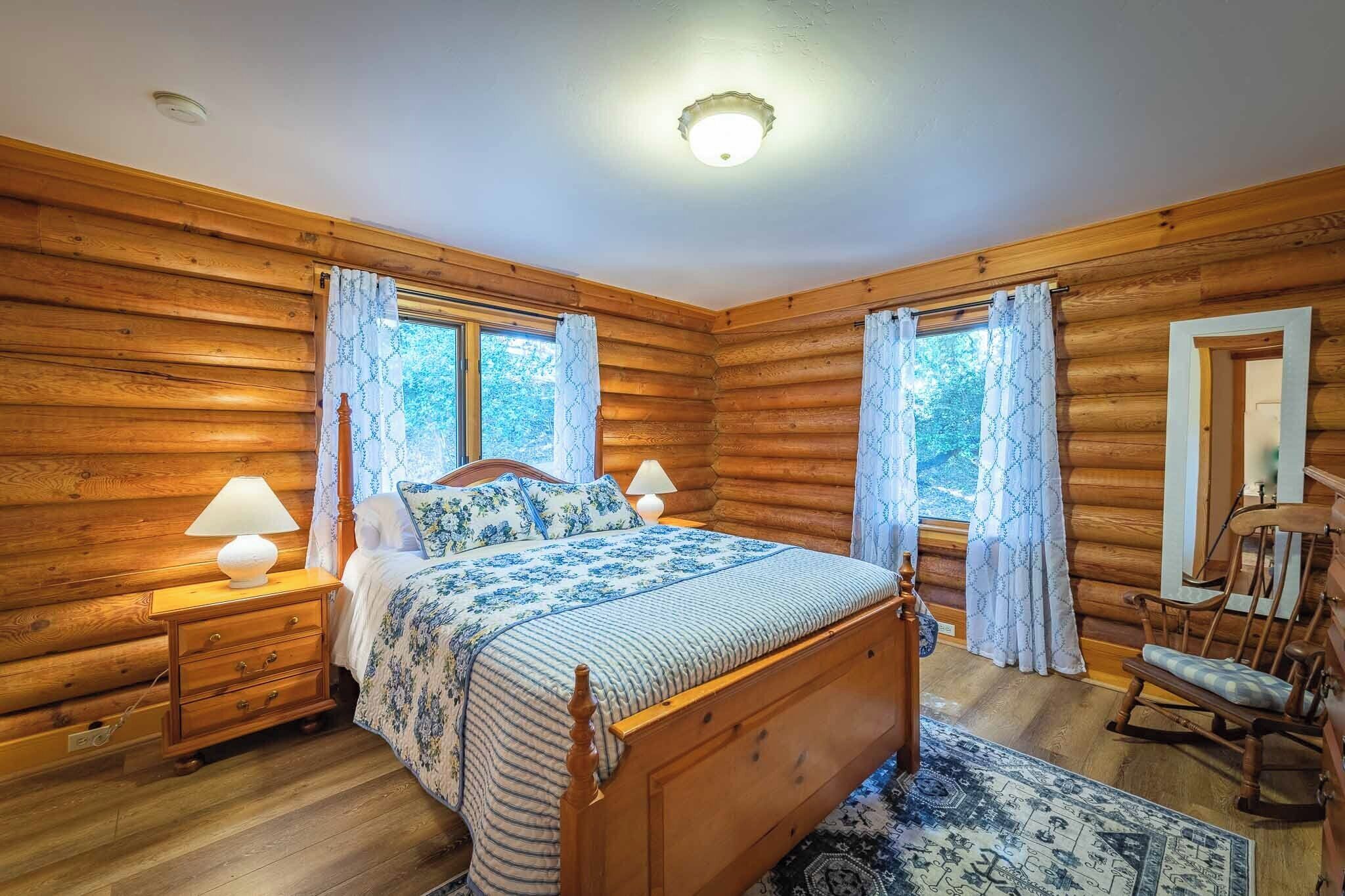 A wooden cabin bedroom with a bed, nightstands, and a rocking chair.