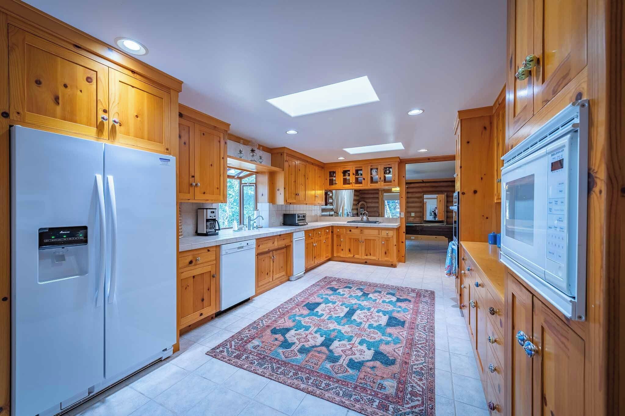 A spacious kitchen with wooden cabinets, a refrigerator, a microwave, and a patterned rug.