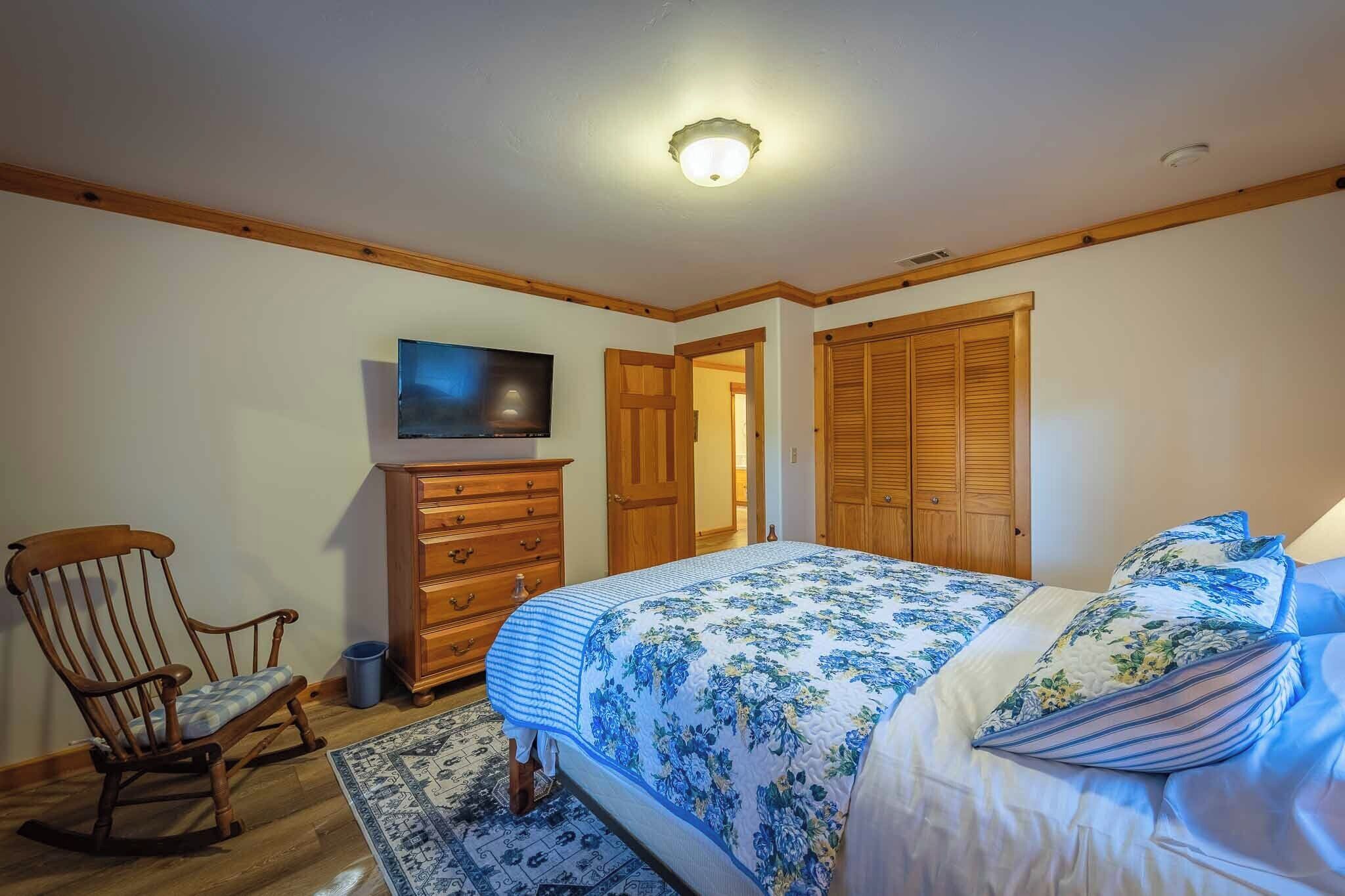 Un dormitorio con una cama, un sillón mecedor de madera, un aparador, un televisor y un armario.