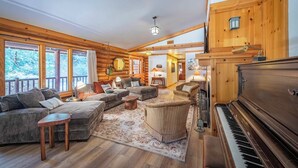 A cozy log cabin interior with a grand piano, a sectional sofa, and a rustic dining area. - Oakwood Lodge (Nipomo)