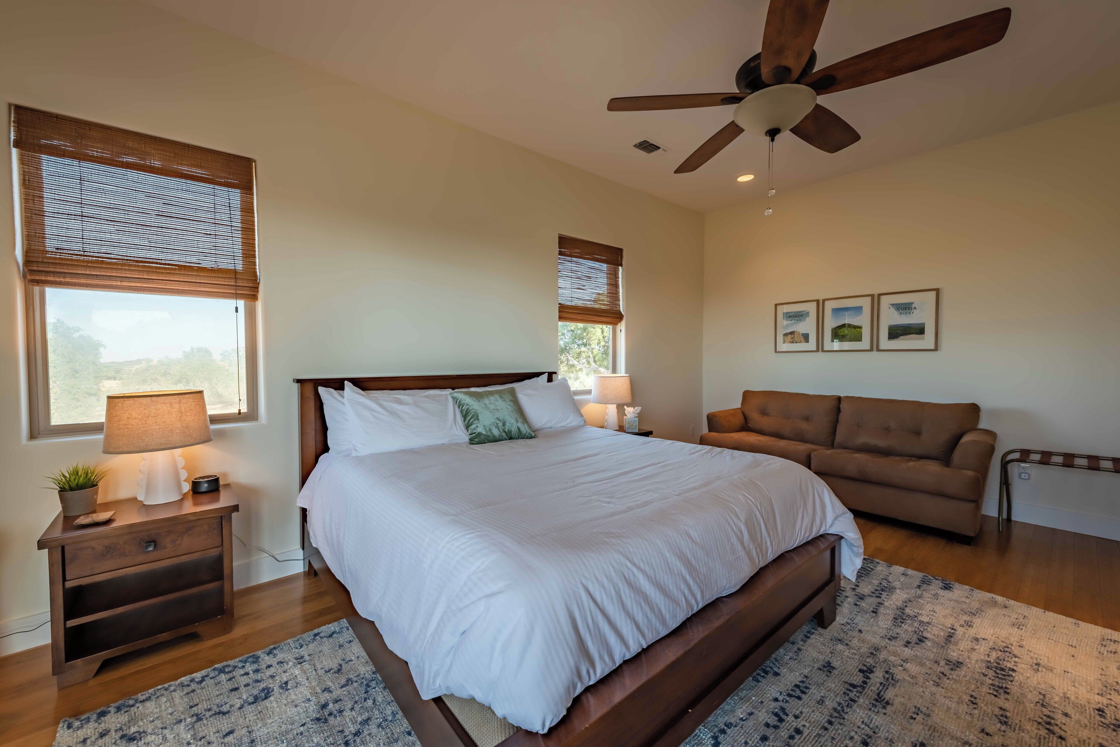 A bedroom with a large bed, wooden nightstands, a ceiling fan, and a brown sofa.