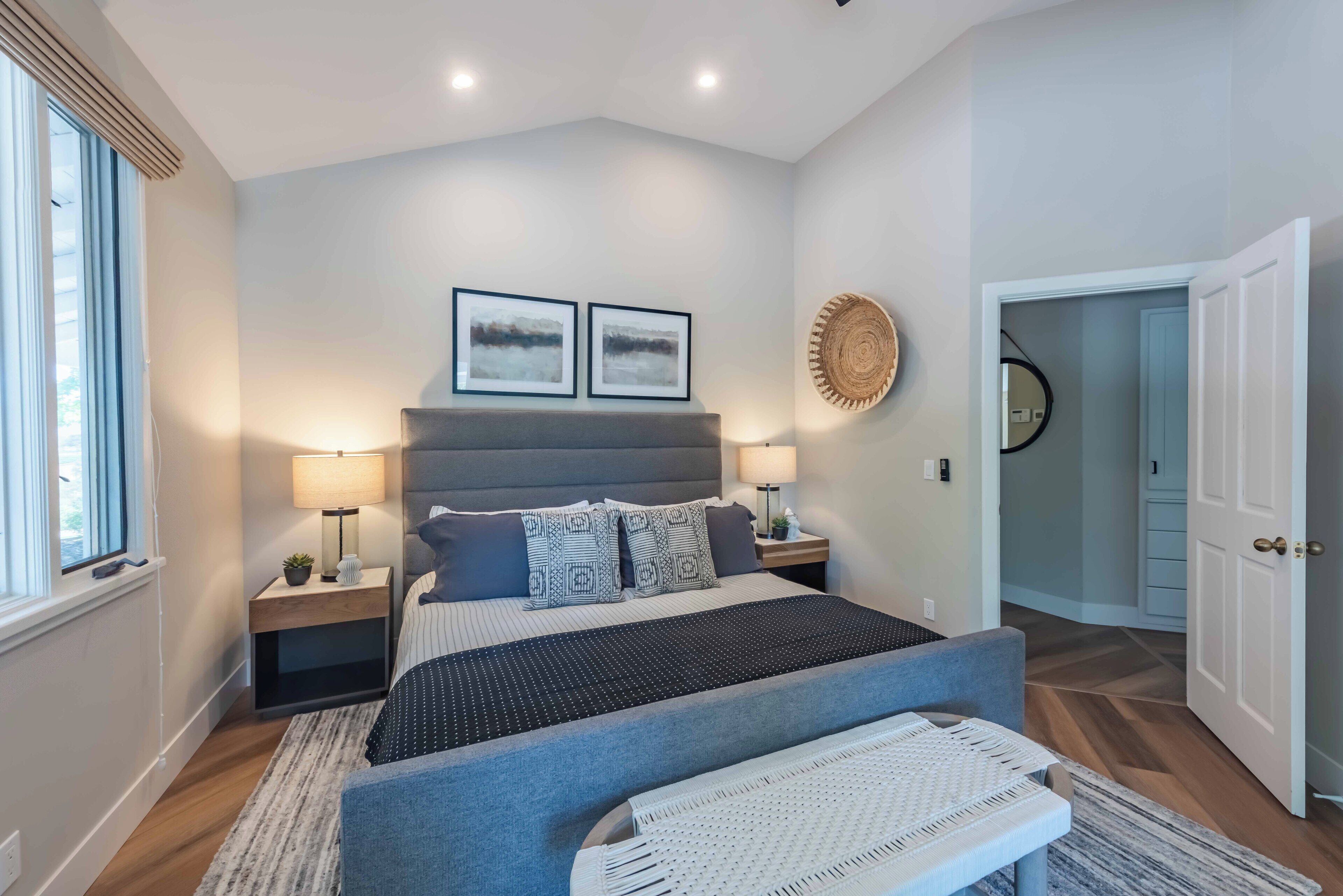 A modern bedroom with a large bed, bedside lamps, a wall-mounted artwork, and a woven wall decoration.